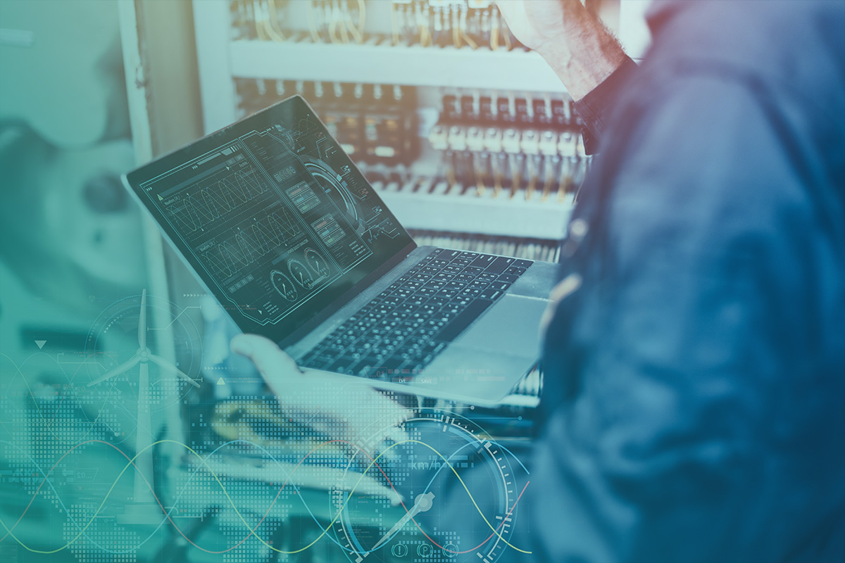 “Engineer reviewing digital system data on a laptop in front of electrical panels, representing Energy Management and performance optimisation.”