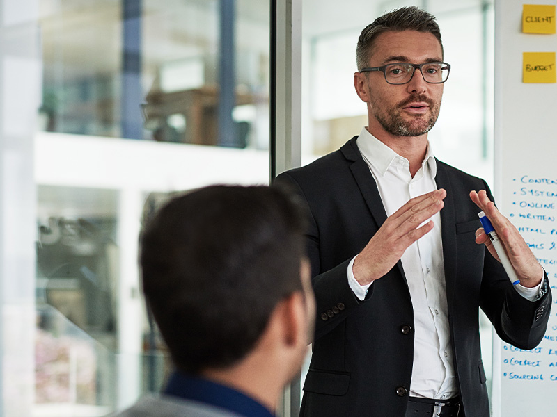 Business professional presenting to colleagues in a meeting, discussing next steps and strategic choices around basket energy procurement.