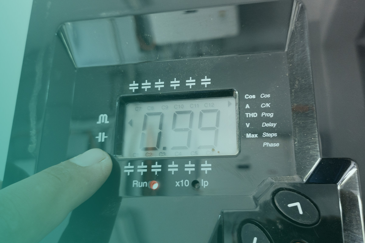 “Engineer adjusting an electrical control unit displaying a 0.99 reading as part of Power Factor Correction.”