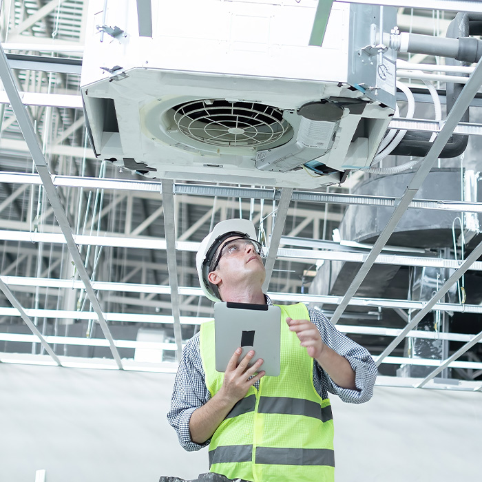 Engineer performing a tm44 inspection on a ceiling-mounted air conditioning unit using a digital tablet.