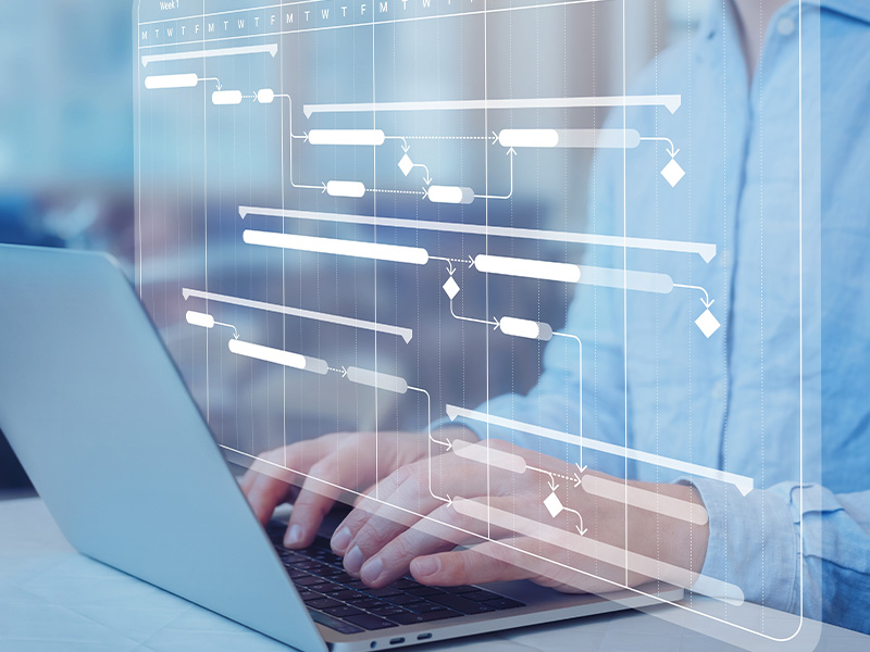 Person working on a laptop with a digital project timeline overlay, symbolising structured delivery of AMR energy meters and BMS audits.