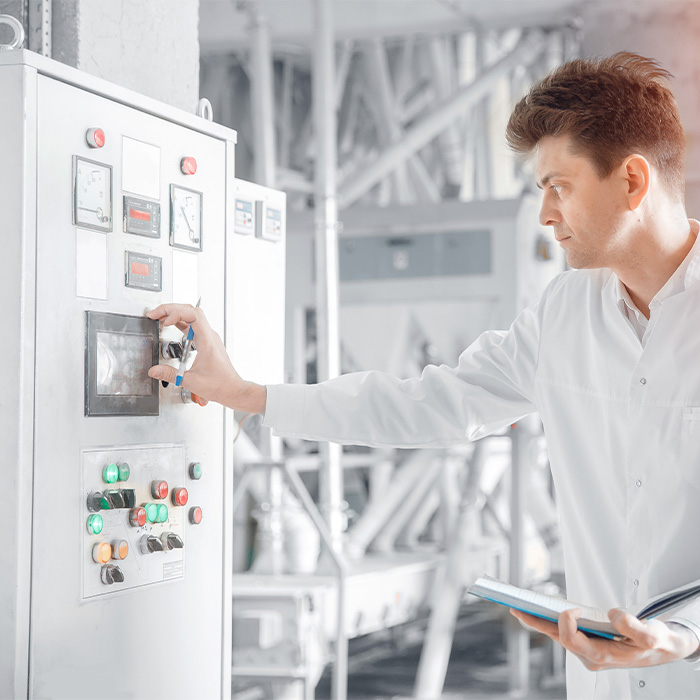Engineer conducting an Energy audit by inspecting industrial control panels and recording data.