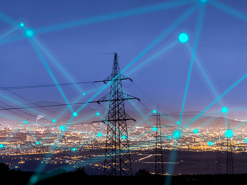 Electricity pylons connected by digital glowing lines over a cityscape, symbolising how AMR energy meters and BMS audits improve energy data quality.