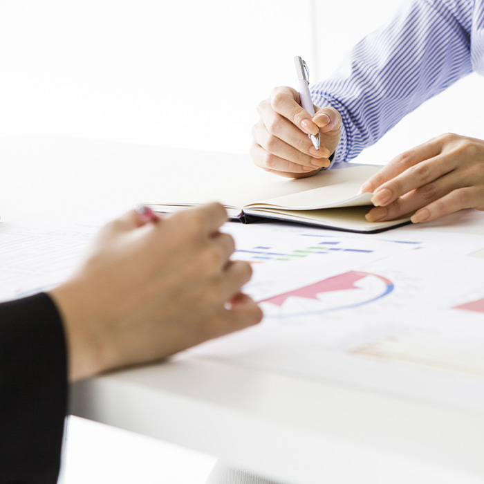 Close-up of professionals reviewing reports and taking notes during a meeting, symbolising expert delivery of a track and trace survey for commercial buildings.