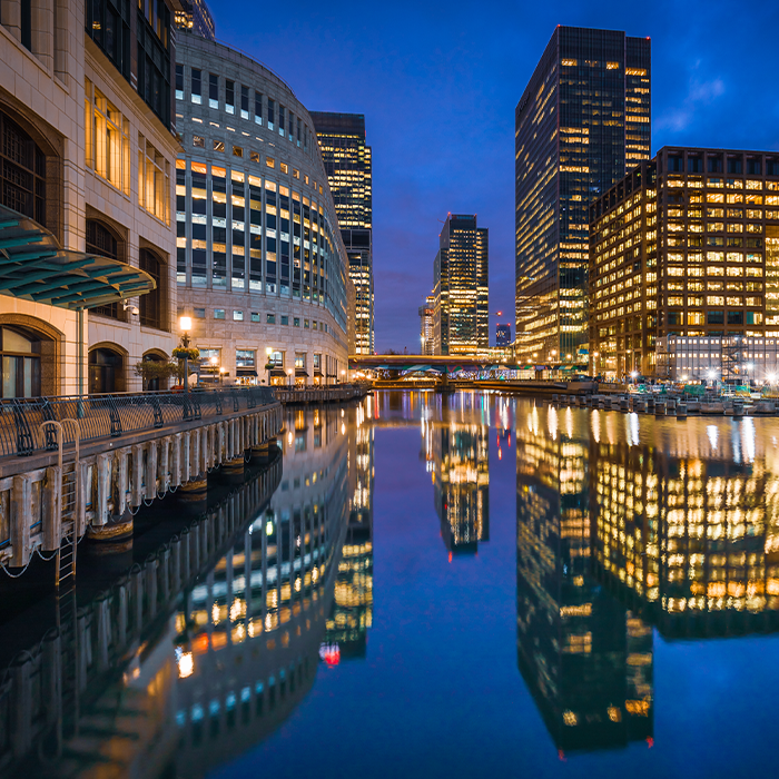 Night view of modern office buildings reflecting in a calm city canal, representing the energy needs met by business electricity providers.