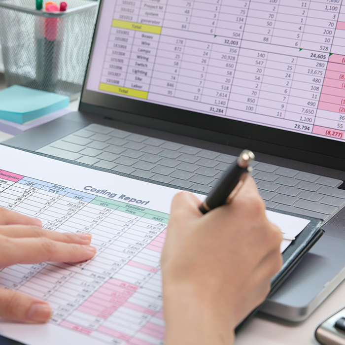 Person reviewing a printed costing report alongside a financial spreadsheet on a laptop, evaluating options from business electricity providers.