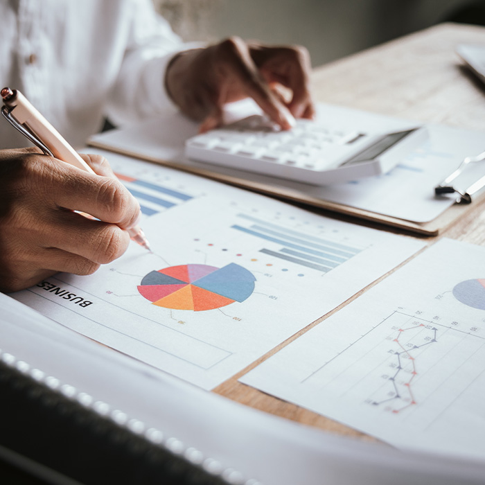 Close-up of a person analysing colourful pie charts and bar graphs with a pen and calculator, representing risk-managed procurement strategies.