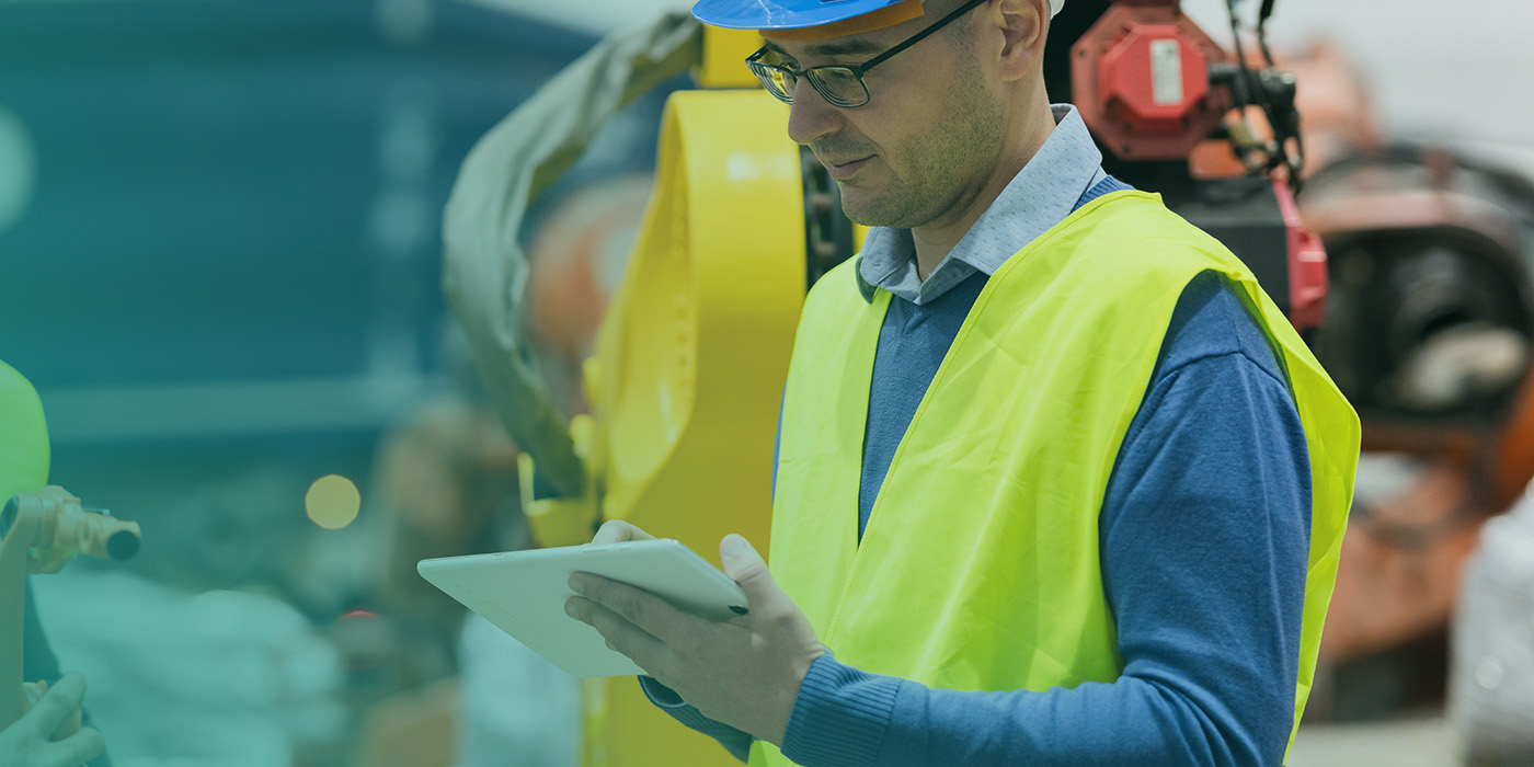 Engineer in high-visibility PPE using a digital tablet on a factory floor, illustrating the impact of well-managed MOP DC DA AMR Contracts on accurate metering and reliable energy data.